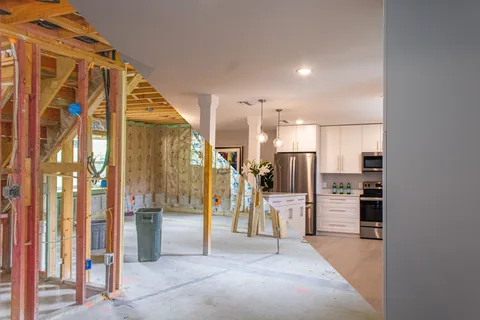 Diagonal before-and-after collage showing exposed wall framing beside a finished white kitchen.