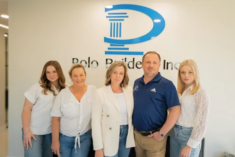 Five people standing beneath the blue Polo Builders logo in an office.