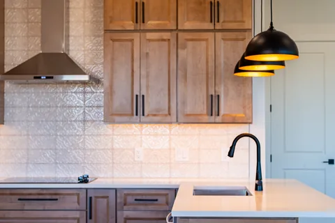 Kitchen with wood cabinets, a patterned backsplash, black pendant lights, and a white sink island.