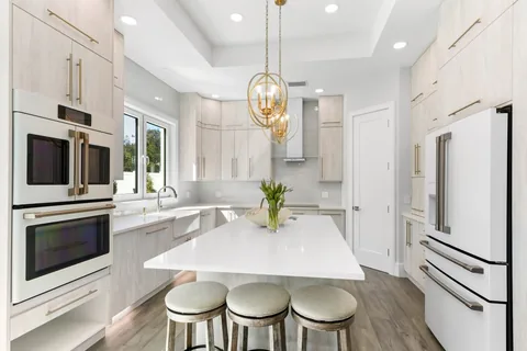 Bright kitchen with cream cabinets, a white island, three round stools and gold pendant lights.