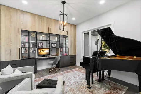 Home office with built-in shelving and a desk beside a black grand piano.